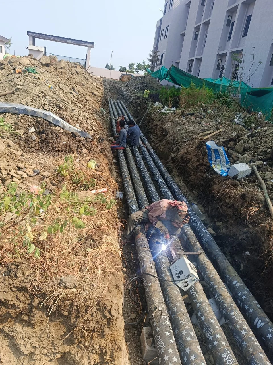 Workers installing underground fire piping beside a building